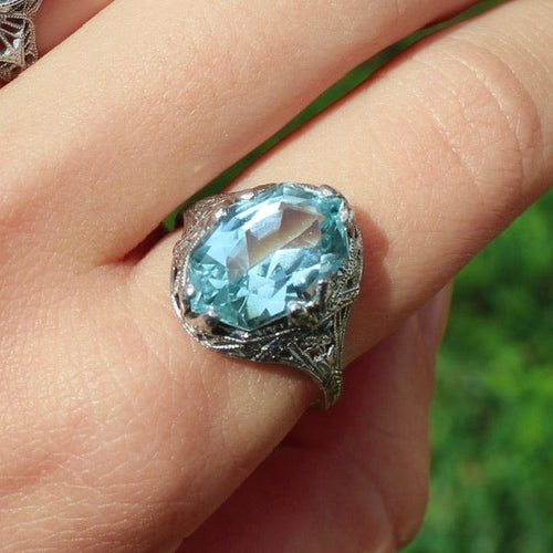 Hand wearing two rings with blue gemstones against a green grass background